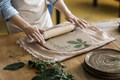 Hands of craftsperson rolling leave on clay with pin at art studio