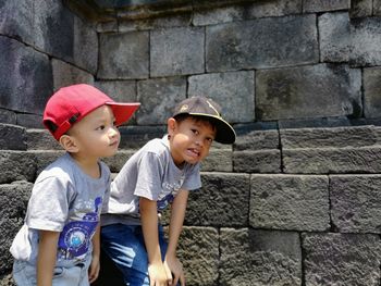 Siblings standing against stone wall