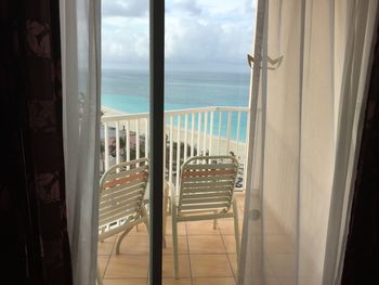 Chairs in balcony against sea seen through window