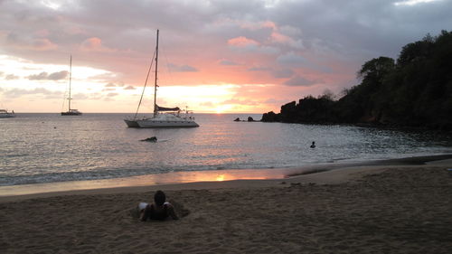 High angle view of man relaxing at beach against cloudy sky during sunset