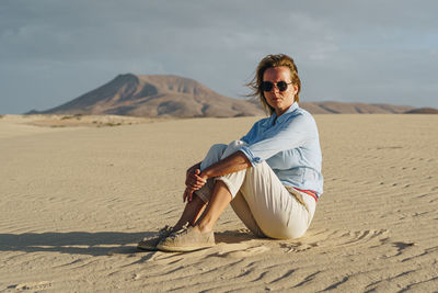 Young man wearing sunglasses on sand at beach against sky
