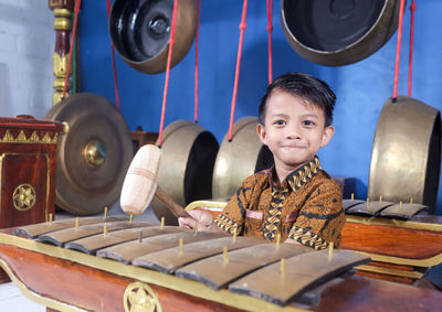 Portrait of smiling boy holding hammer sitting by musical instrument