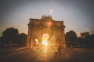 People walking against triumphal arch in city during sunset