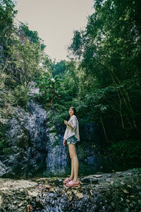 Full length of woman standing on rock in forest