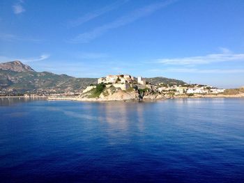 Scenic view of sea by buildings against blue sky