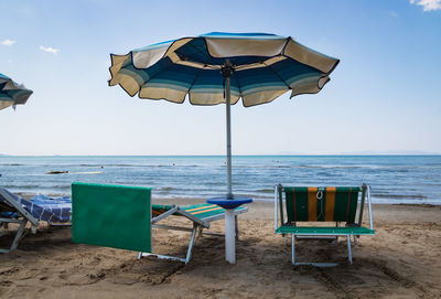 Deck chairs on beach against sky