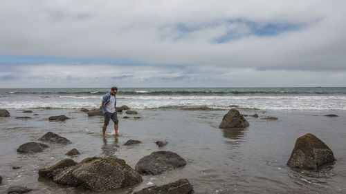 Full length of man standing on rock at beach against sky