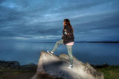 Young woman standing on rock by sea against sky