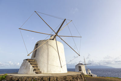 Traditional windmill by sea against sky