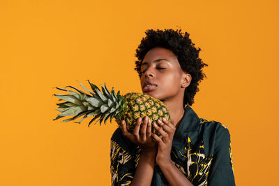 Young african american woman with short hair dressed in a summer shirt posing with pineapple