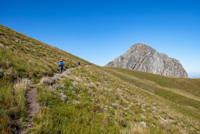 People riding on mountain against clear blue sky