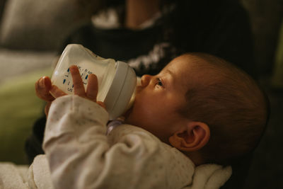 Midsection of mother feeding milk bottle to daughter at home