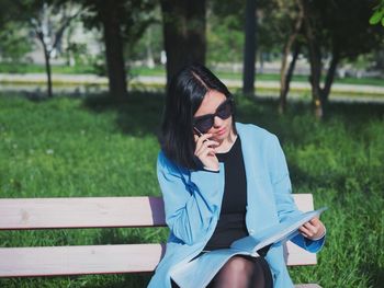 Woman reading document while sitting on bench at park