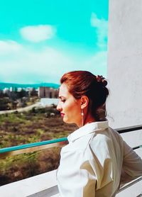Young woman looking away while standing against railing