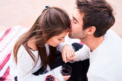 From above cheerful young couple in casual wear toasting with glasses of red wine while enjoying happy moments together