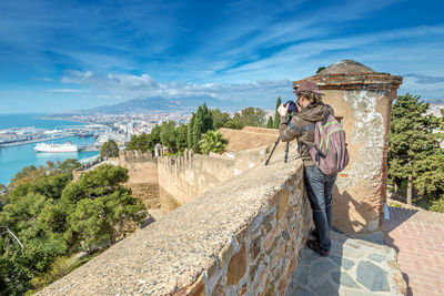 Rear view of man photographing from observation point against blue sky