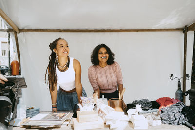 Smiling female owner looking away while standing in stall at flea market