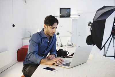 Male blogger using laptop at desk in creative office