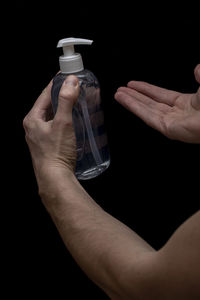 Cropped image of man holding bottle against black background