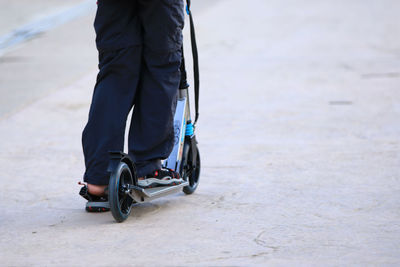 Low section of man riding push scooter on road