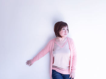 Woman looking away standing against white wall