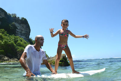 Man teaching girl to surf in sea