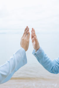 Cropped hand of couple gesturing against sea