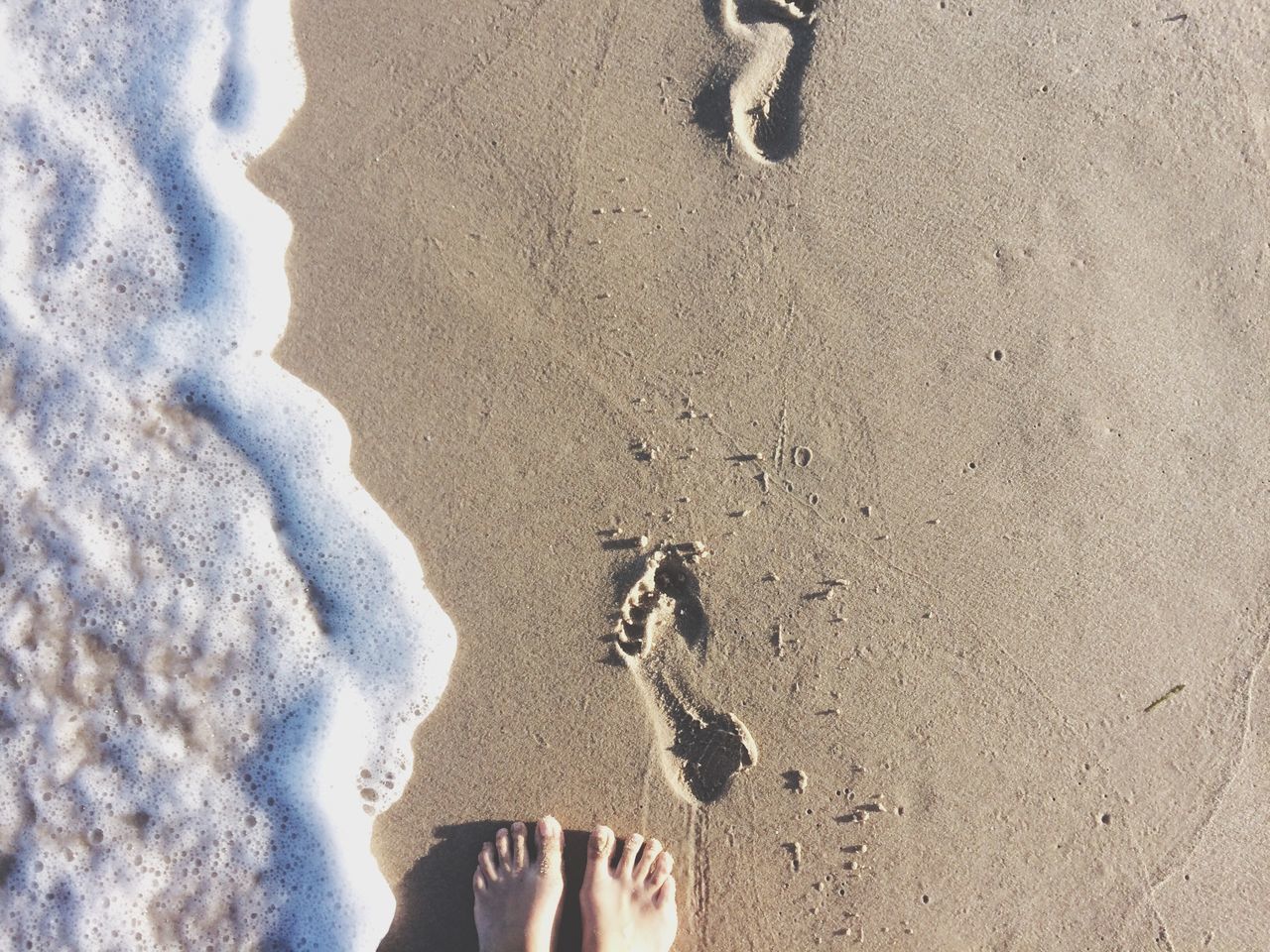 low section, person, personal perspective, beach, standing, human foot, sand, lifestyles, high angle view, leisure activity, shoe, unrecognizable person, shore, barefoot, footprint, water, outdoors