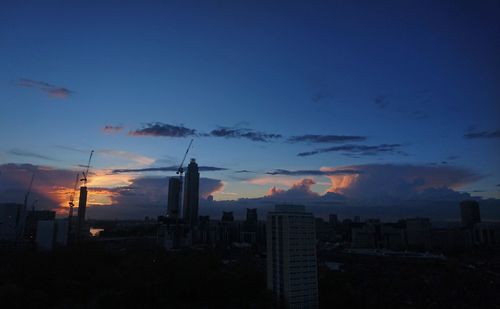 Silhouette of city against cloudy sky during sunset