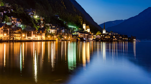 Illuminated houses by sea against sky at night