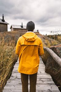 Rear view of man standing on yellow umbrella against sky