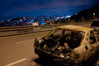 Abandoned car on city street against sky at night