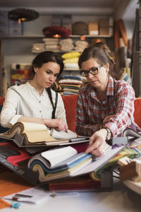 Owner showing fabric swatches to female customer while sitting at store