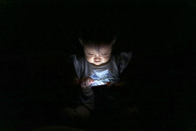 Cute baby girl using mobile phone in darkroom