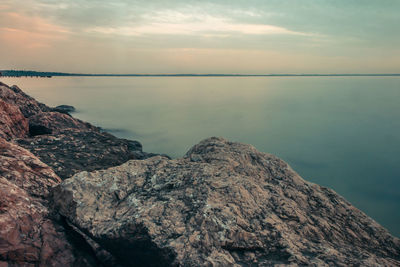 Rocks by sea against sky during sunset