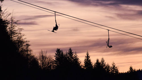 Low angle view of silhouette man hanging on rope against sky
