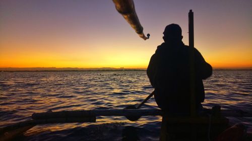 Rear view of silhouette man standing at beach against sky during sunset