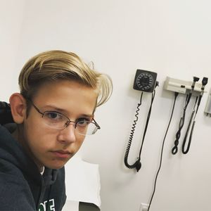 Close-up portrait of young man with eyeglasses against wall