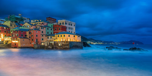 Illuminated buildings by sea against sky at dusk