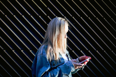 Side view of woman using mobile phone against wall