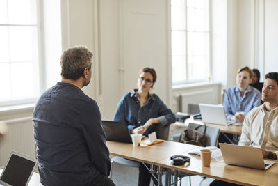 Rear view of male teacher teaching students in classroom