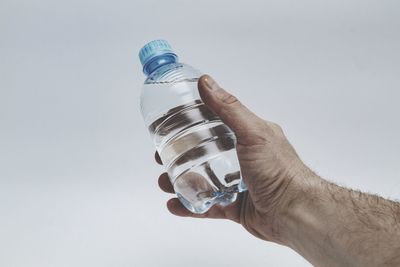 Close-up of hand holding glass bottle against white background