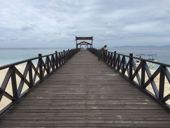 Side view of man leaning on pier over sea against cloudy sky