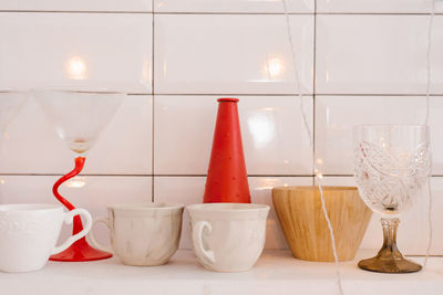 White porcelain or ceramic mugs, wooden crockery, red vase and wine glass on the kitchen shelf