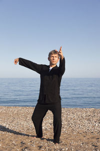 Full length of man exercising at beach against clear sky