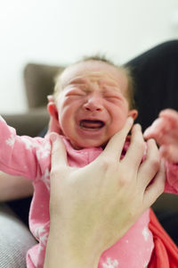 Newborn baby girl in pink pajamas held upright cries in mother's hands
