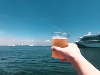 Hand holding glass of water against sky