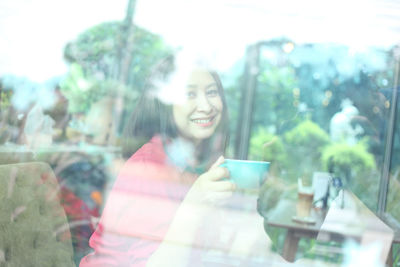 Portrait of smiling young woman seen through glass window