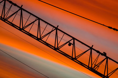 Low angle view of silhouette metallic tower against orange sky