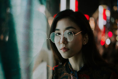 Portrait of young woman standing against illuminated city at night